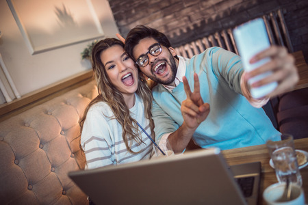  Beautiful loving couple sitting in a cafe drinking coffee and using phone, make selfie. Love and romance concept.の写真素材