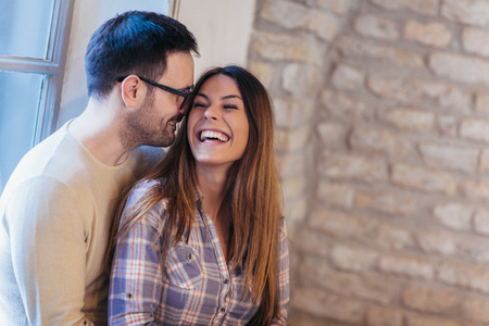 Portrait of a young couple hugging next to the window, brick wall background.の写真素材