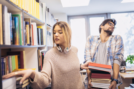 people, knowledge, education and school concept - happy student couple with books in libraryの写真素材