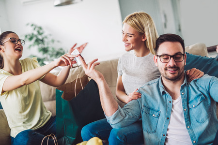 Two women and a man in a living room holding a credit card and shopping bagsの写真素材