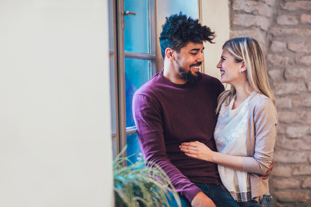 Portrait of a young couple hugging next to the window, brick wall background.