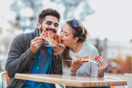 Couple eating pizza outdoors and smiling.They are sharing pizza in a outdoor cafe.の写真素材