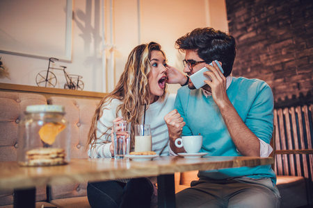  Beautiful loving couple sitting in a cafe drinking coffee and using phone. Love and romance concept.の写真素材