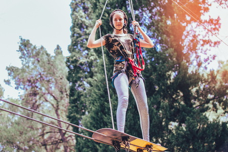 Happy school girl enjoying activity in a climbing adventure park on a summer day
