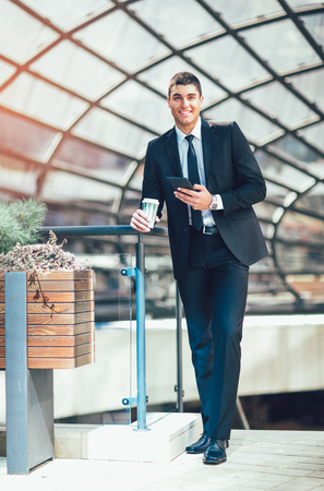 Young business man with formal suit using digital tablet and drink coffee outdoor. business, technology conceptの写真素材