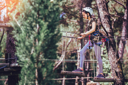 Happy school girl enjoying activity in a climbing adventure park on a summer day
