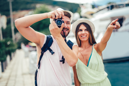 Couple of tourists taking a walk in a city street sidewalk in a sunny day, laughing and having fun.の写真素材
