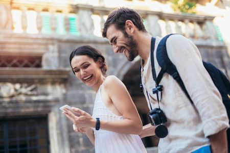 Traveling couple of tourists walking around old town, and using smart phone. Vacation, summer, holiday, tourism: concept.の写真素材