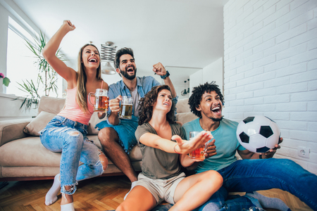Happy friends or football fans watching soccer on tv and celebrating victory at home.Friendship, sports and entertainment concept.の写真素材