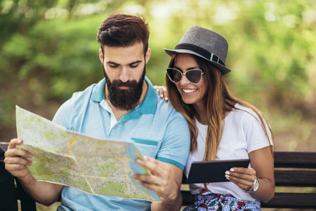 Happy tourist couple looking at map on a bench in the park on a sunny dayの写真素材