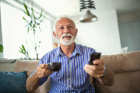 Senior man enjoys watching tv at home.Senior man watching tv and drink coffeeの写真素材