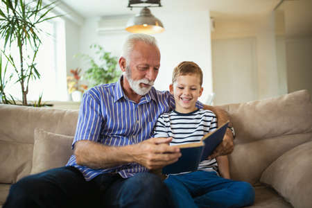 Grandfather With Grandson Reading Together On Sofaの写真素材