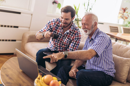 Adult Son Helping Senior Father With Computer At Homeの写真素材