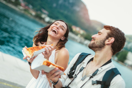 Happy couple of tourist eating pizza on street near the seaの写真素材