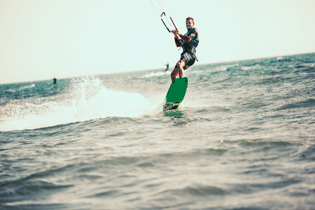 Professional kiter makes the difficult trick on a beautiful background. Kitesurfing Kiteboarding action photos man among waves quickly goesの写真素材
