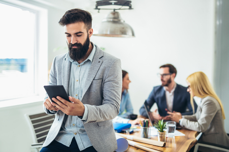 Portrait of young businessman using digital tablet while colleague in backgroundの写真素材