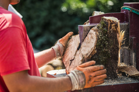 A man working with the firewood to split the logs by the machine on the driveway in the gardenの写真素材