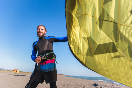 Handsome Caucasian man professional surfer standing  on the sandy beach with his kite