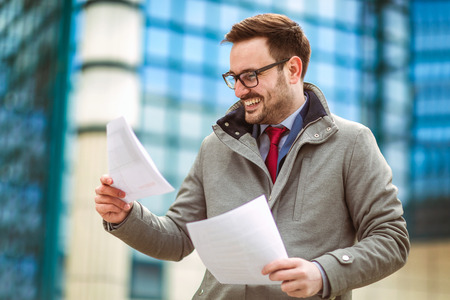 Young attractive businessman holding documents, papers. Young concentrated man reading documents, ...