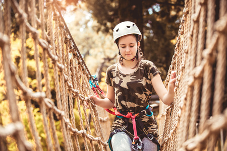 Happy school girl enjoying activity in a climbing adventure park on a summer day