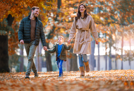Young family walking in the autumn park with his son, holding his hand.の写真素材