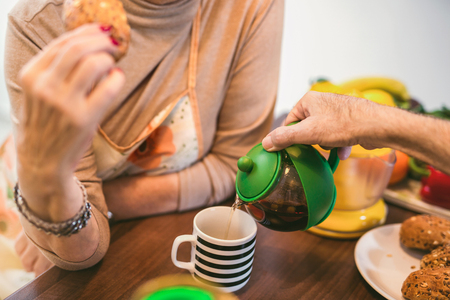 Elderly couple in the kitchen preparing breakfast. They drink coffee or tea and talkの写真素材