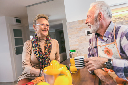 Elderly couple in the kitchen preparing breakfast. They drink coffee or tea and talkの写真素材