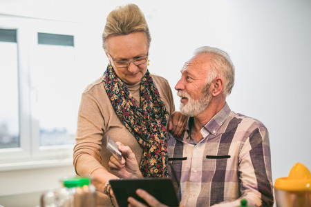 Senior couple using digital tablet and credit card in the kitchen at home for online shoppingの写真素材