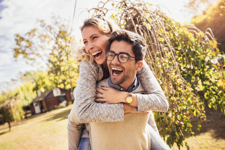 Couple having fun man giving piggyback to woman in autumn parkの写真素材