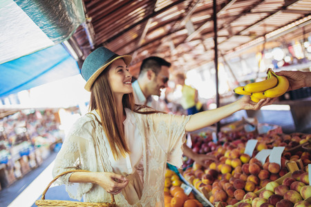 Young couple buying fruits and vegetables in a market on a sunny morning.の写真素材