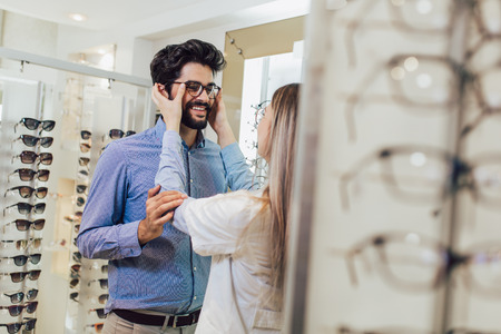 Femaale ophthalmologist helping man to choose glasses in optical store