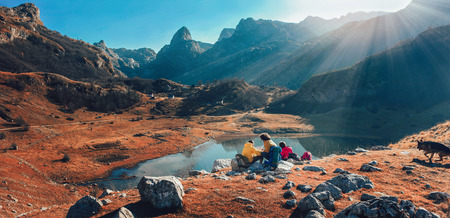 Panorama view on group of hikers enjoying view on mountain lake. Young people hiking in nature