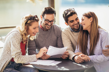 Group of four friends having fun a coffee together. Two women and two men at cafe talking laughing and enjoying their timeの写真素材