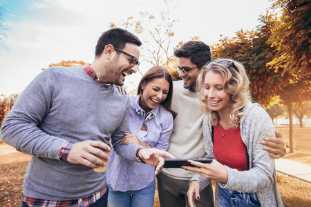 Four happy smiling young friends walking outdoors in the park holding digital tabletの写真素材