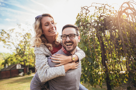 Couple having fun man giving piggyback to woman in autumn parkの写真素材