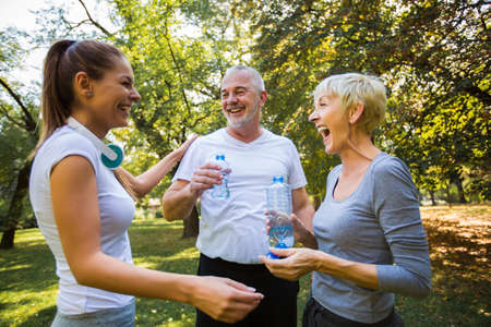 Senior man and woman and young female instructor workout on fresh air, they rest and drink water.の写真素材