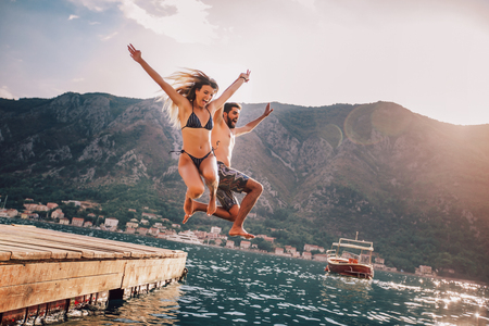Young couple jumping from a pier into the waterの写真素材