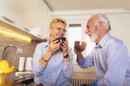 Happy senior man and woman couple sitting together at home smiling and drinking tea or coffeeの写真素材