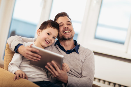 Father and son playing on a tablet at home, having fun, selective focus.の写真素材