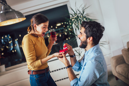 Portrait of a handsome man proposing to his happy girlfriend while holding engagement ring in a boxの写真素材