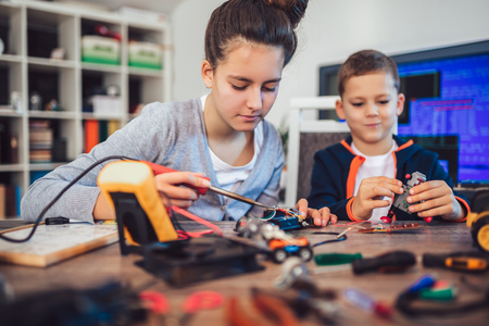 Happy smiling boy and girl constructs technical toy and make robot. Technical toy on table full of detailsの写真素材