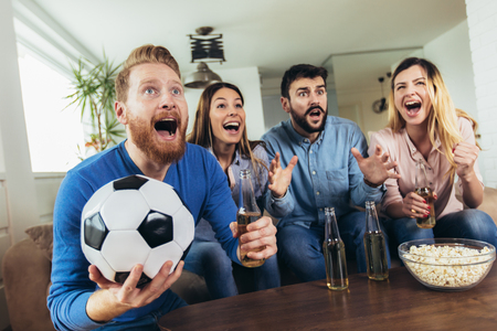 Happy friends or football fans watching soccer on tv and celebrating victory at home.Friendship, sports and entertainment concept.の写真素材