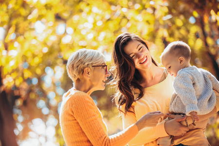 Grandmother and mother smiling at baby in autumn park.の写真素材