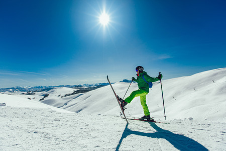 Skier standing with one raised leg on a ski slope at a sunny day and looking somewhere の写真素材