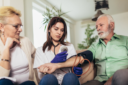Young medic taking blood pressure during home visitの写真素材
