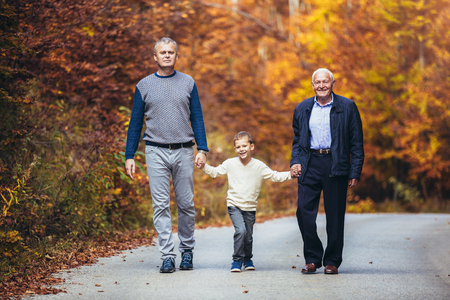 Elderly father adult son and grandson out for a walk in the park.の写真素材