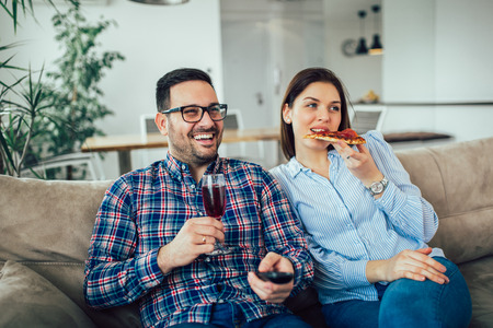 Beautiful young couple eating pizza,talking and smiling at home.の写真素材