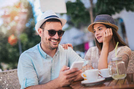 Beautiful loving couple sitting in a cafe enjoying in coffee and using phoneの写真素材