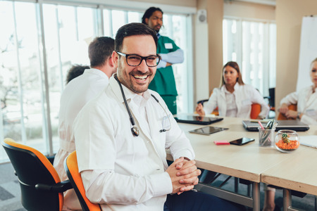 Male doctor with colleagues in background, doctor looking at camera with emergency team in background の写真素材