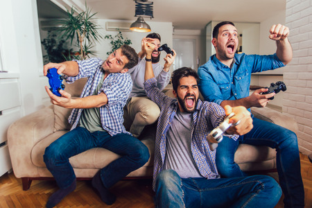 Smiling male friends playing video games at home and having fun.